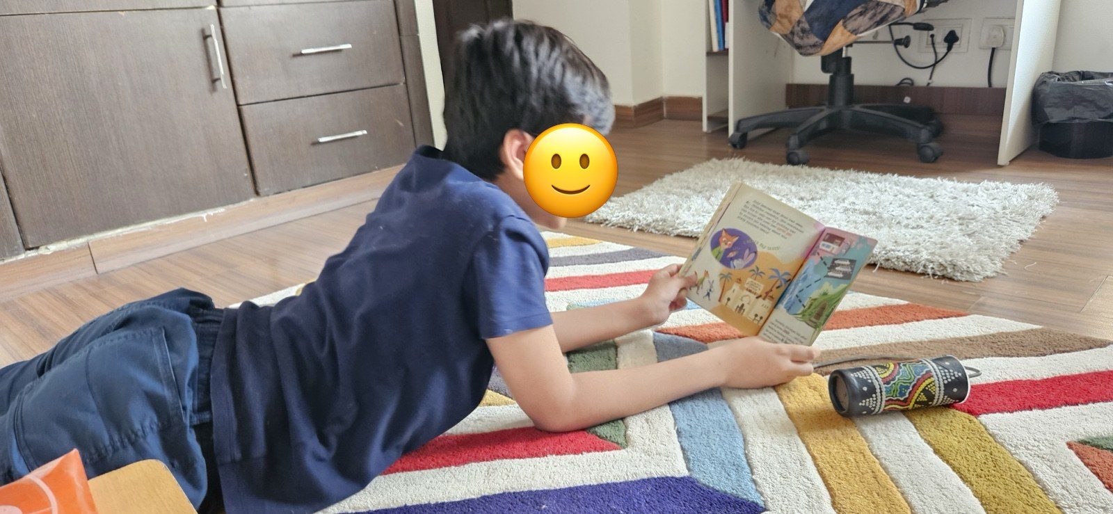A child reading on a colourful rug in Prachi&rsquo;s therapy room, face covered with an emoji