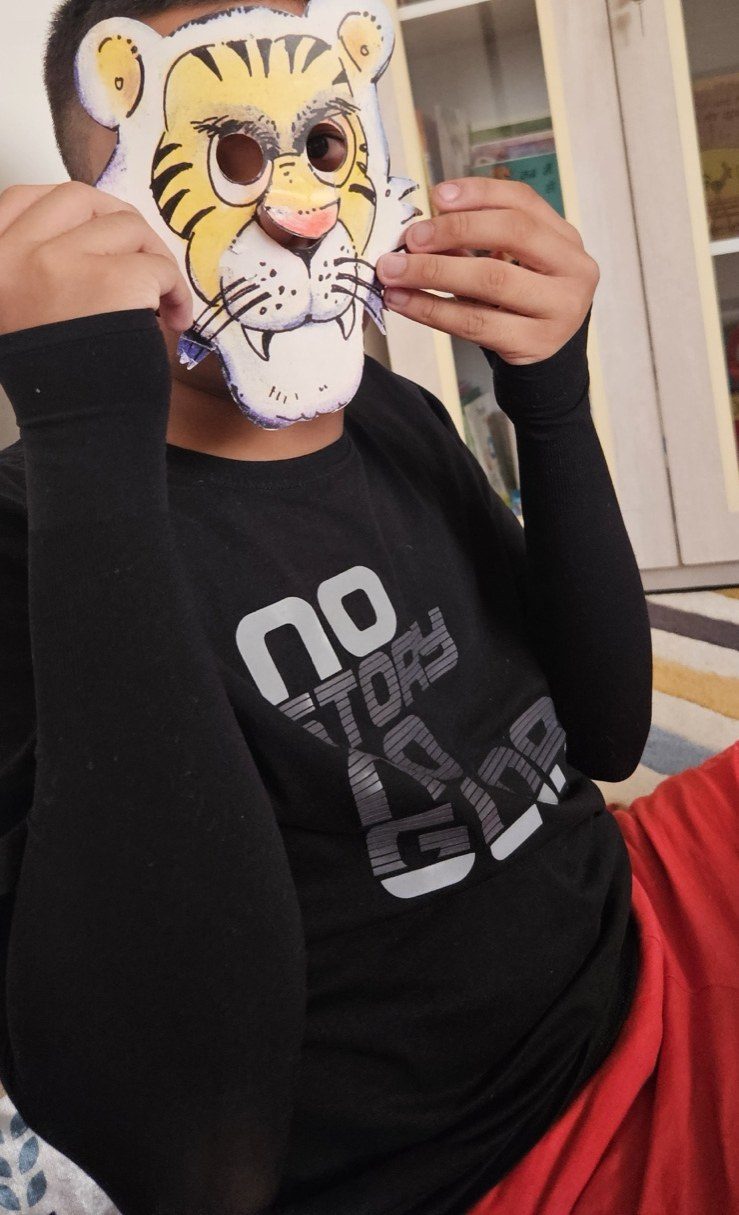 A child holding a hand-painted paper tiger mask up over their face