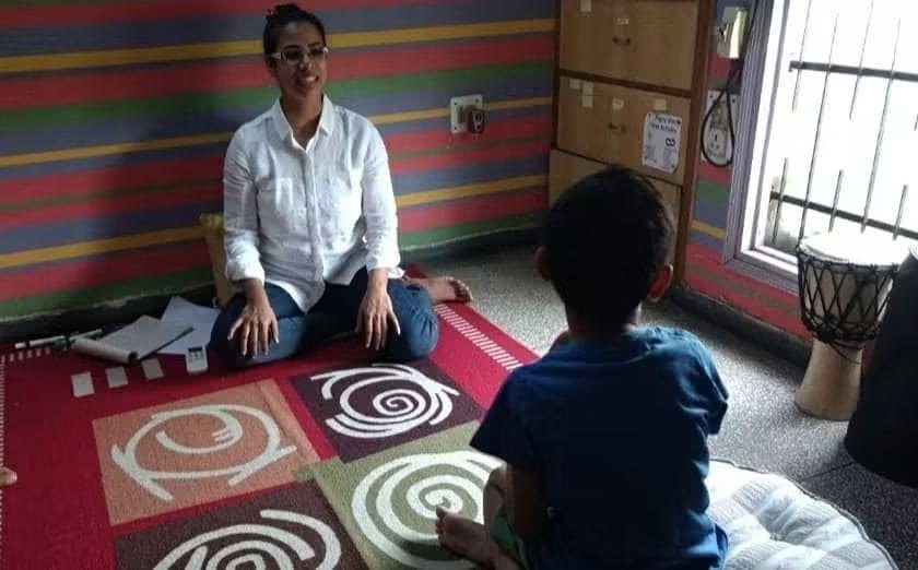 A play therapy session on a spiral-patterned rug: the child leads while Prachi sits cross-legged, listening
