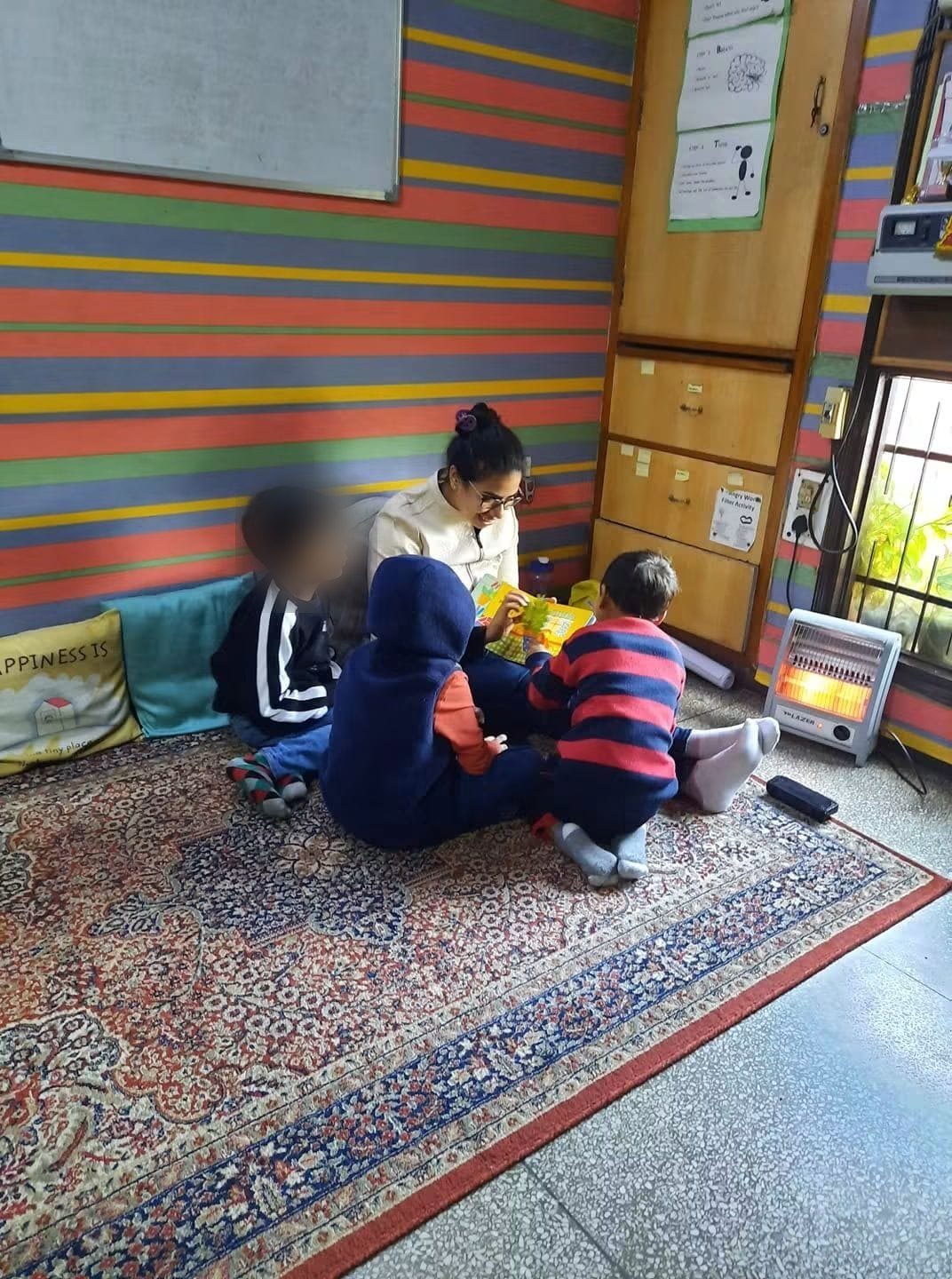 Children absorbed in a group activity on the carpet of a colourful therapy room, with Prachi guiding