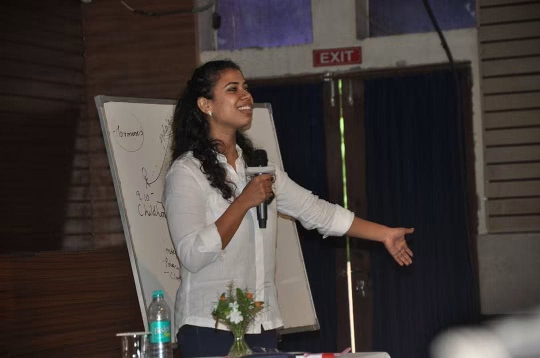 Prachi teaching at a whiteboard during a school workshop, arm outstretched mid-explanation